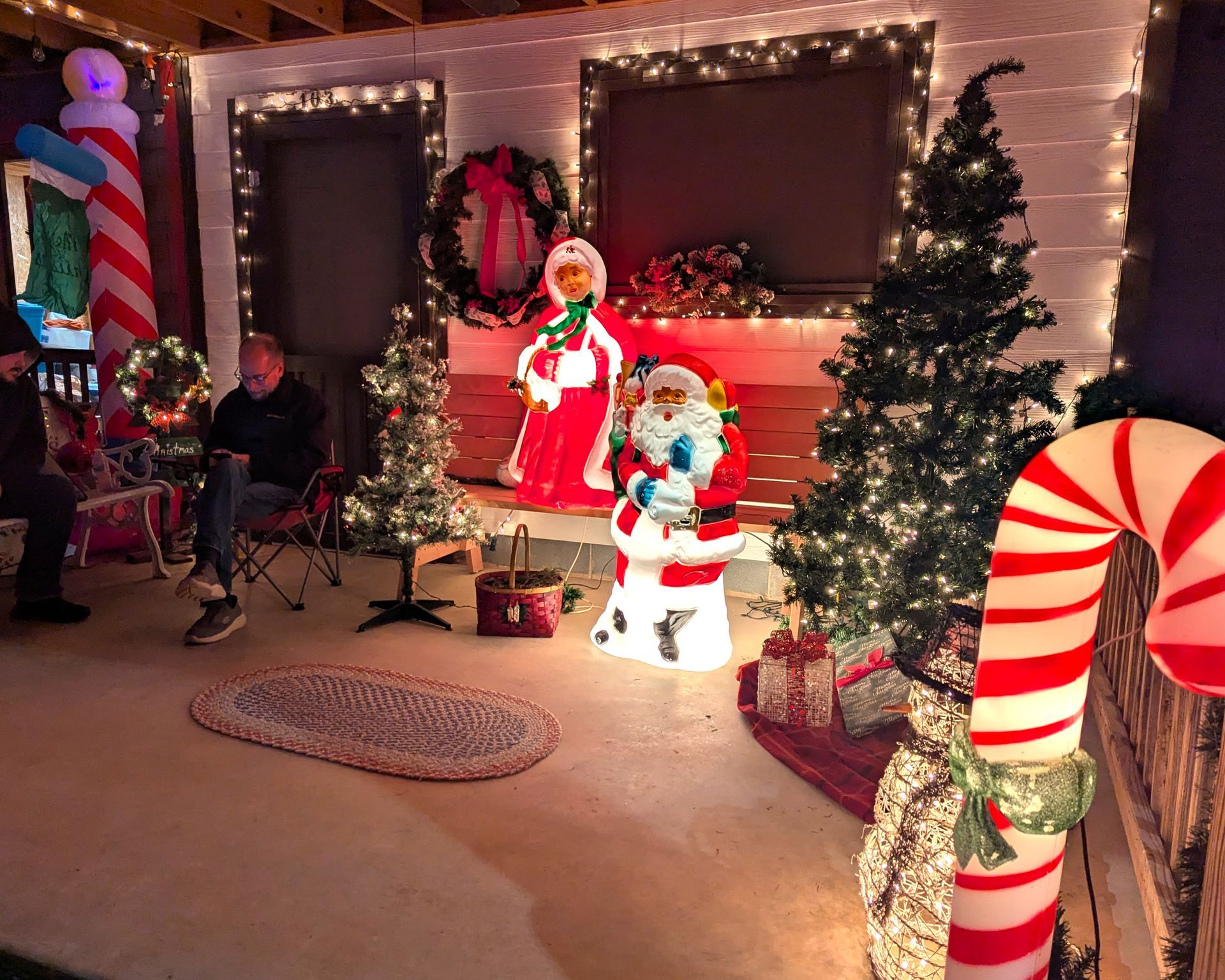 Christmas porch display with lit snowman, Santa figure, wreath, tree, and candy cane decorations