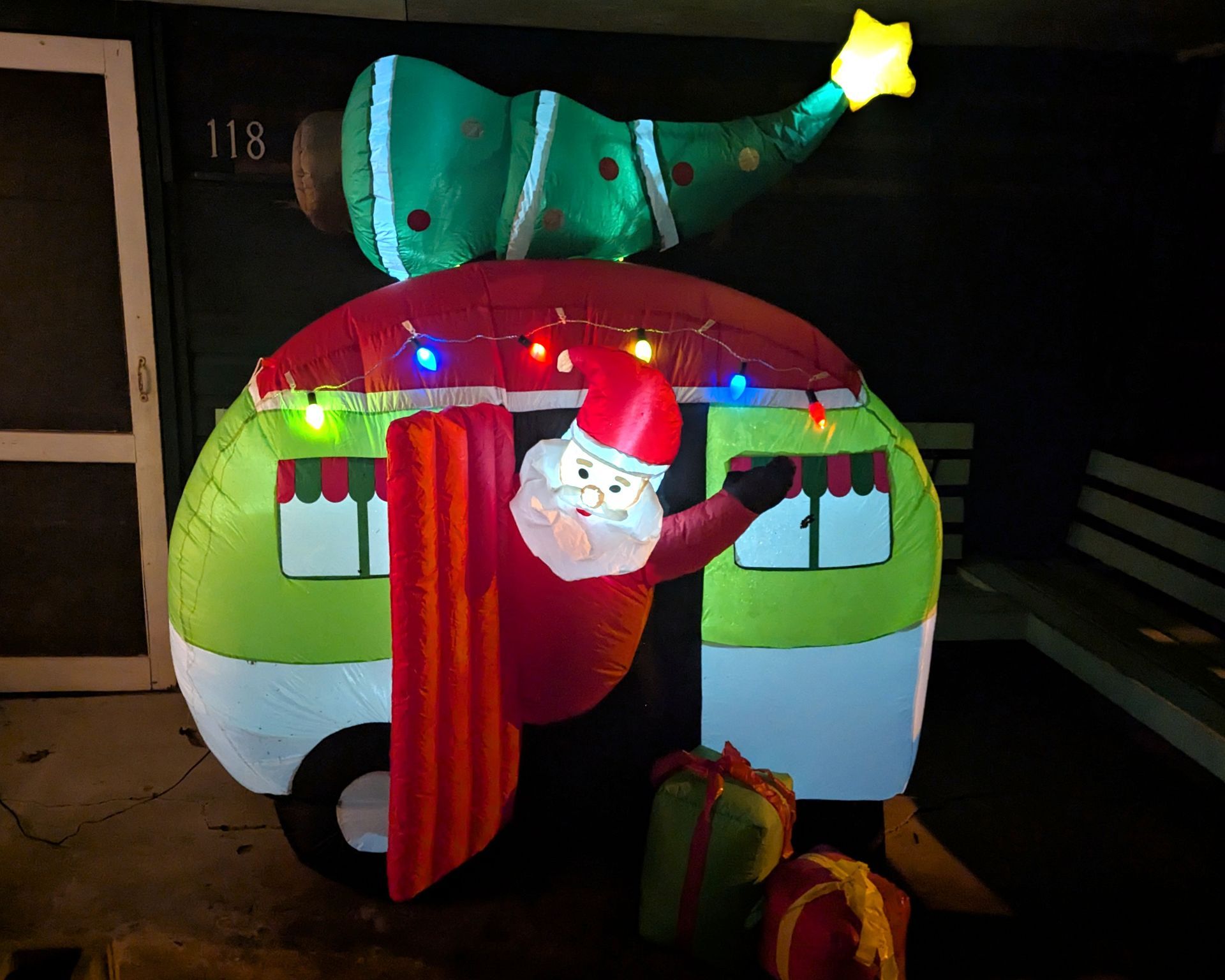 Inflatable holiday Santa peeking from a colorful house with a lit Christmas tree on top at night
