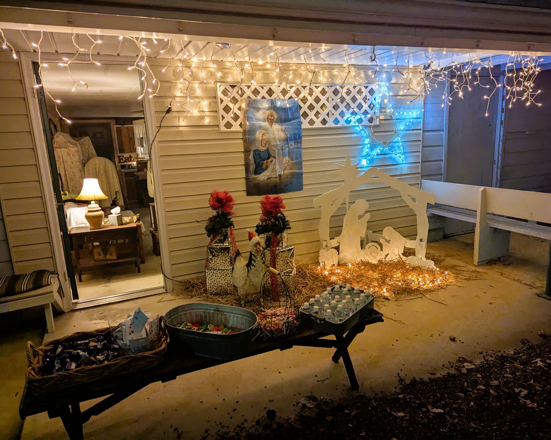 Snowy front porch decorated with warm white lights, blue glow, and holiday ornaments
