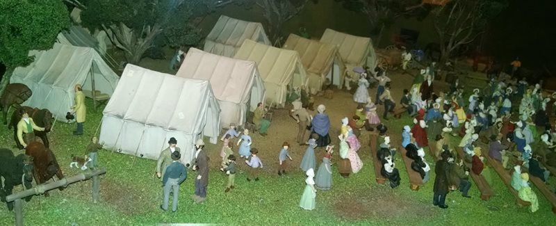 Miniature camp scene with white tents and many tiny figures gathered outdoors at night