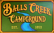 Balls Creek Campground sign in green and gold with a blue wave and “Est. 1853”
