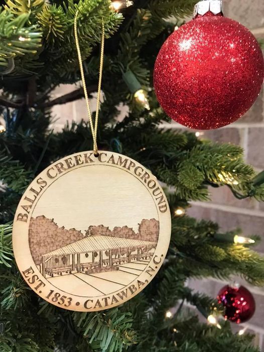 Wooden Balls Creek Campground ornament hanging on a Christmas tree beside a red bauble