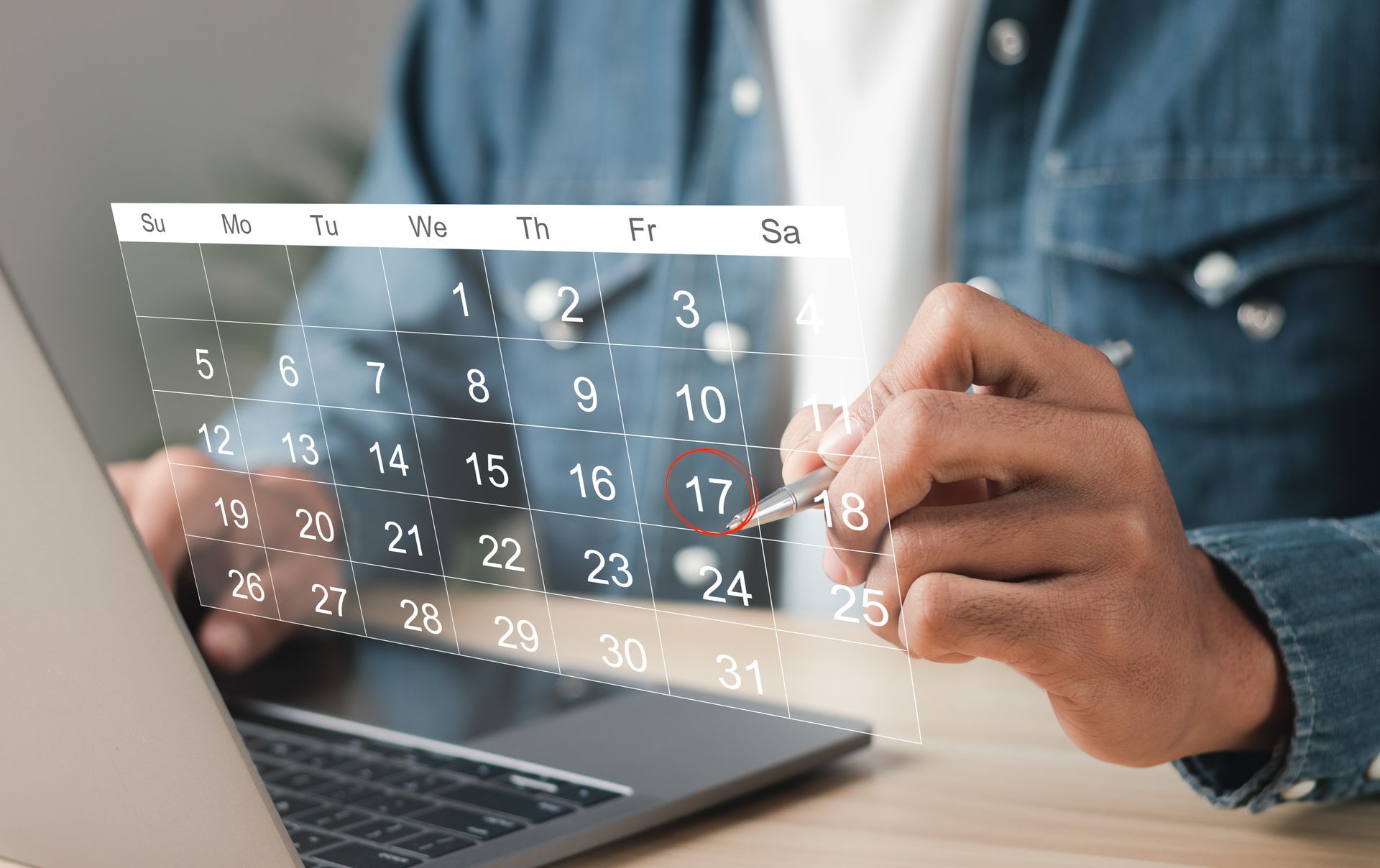 Hands using a laptop with a transparent monthly calendar overlay on the screen