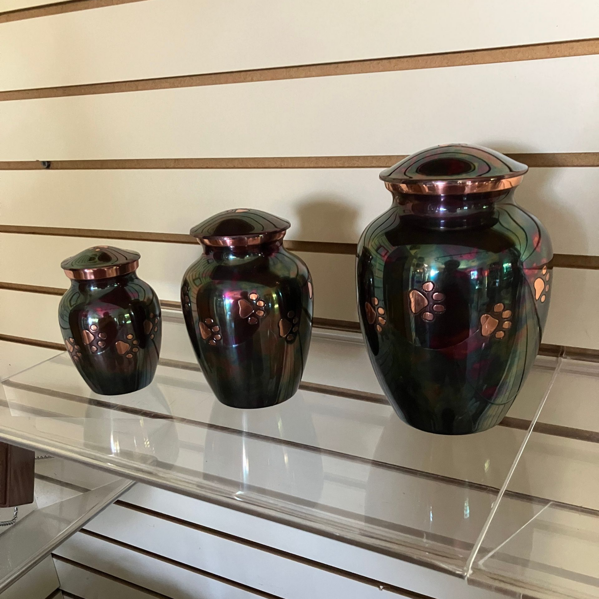 Three glossy dark ceramic vases with floral accents displayed on a glass shelf.