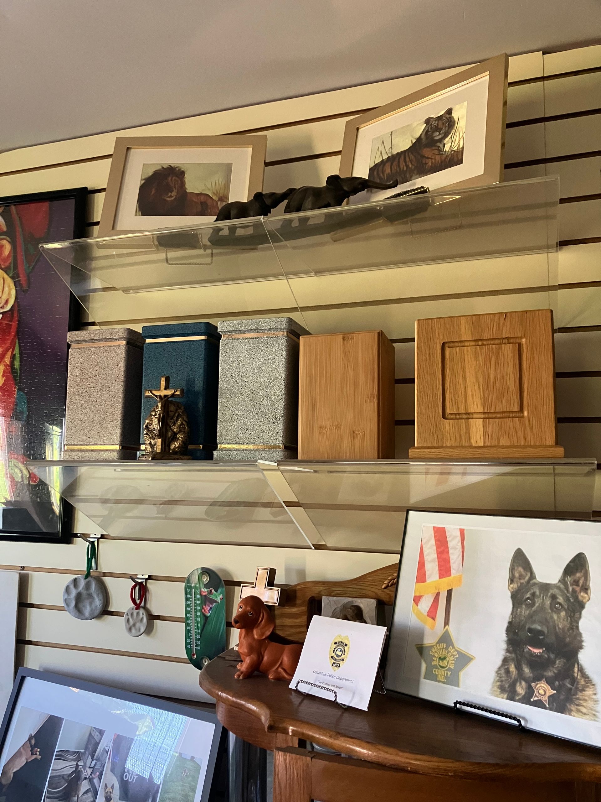 Wall-mounted shelves displaying framed art, wooden boxes, mugs, and a dog portrait in a home interior.