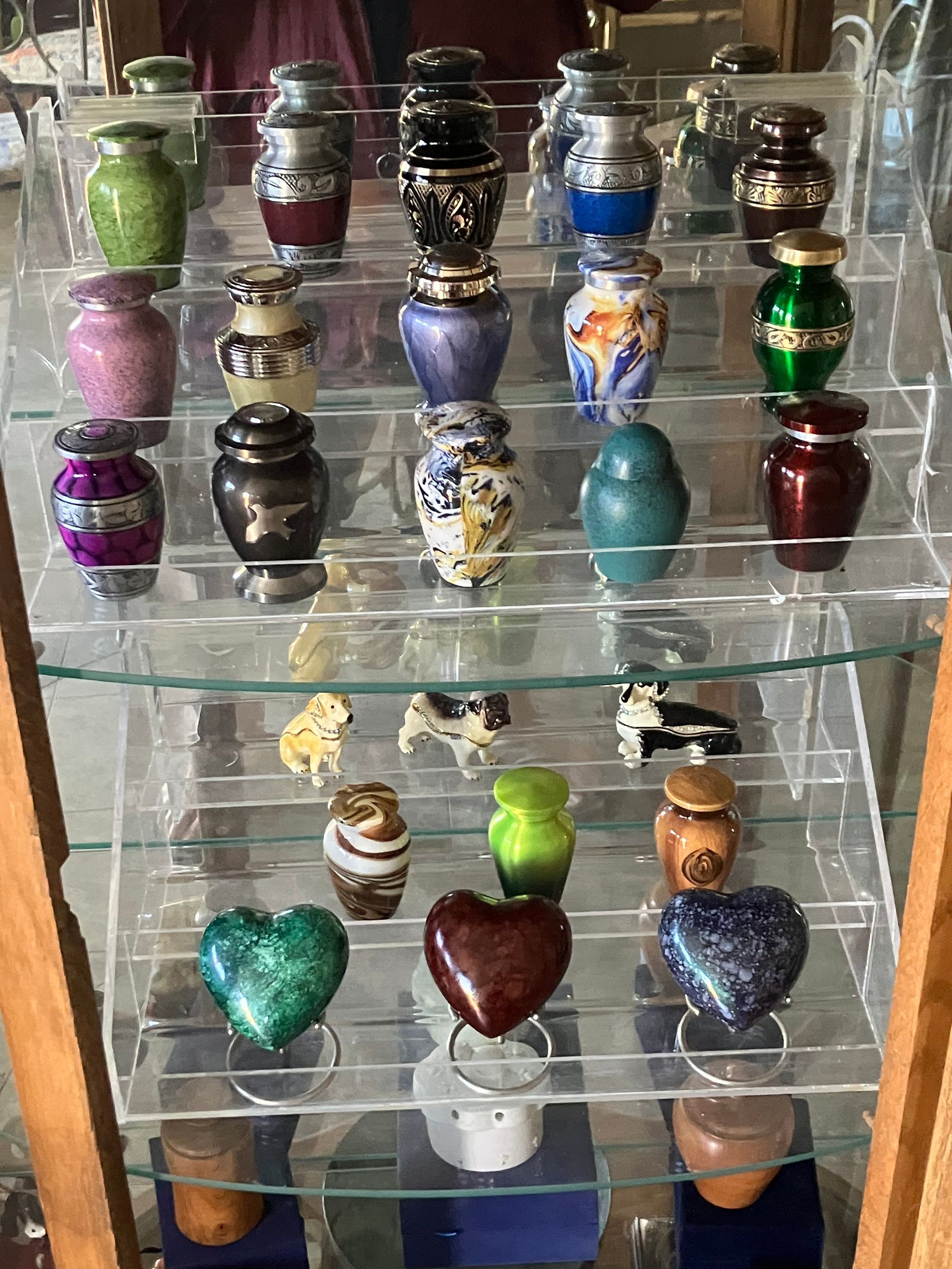 Glass shelf with rows of colorful decorative urns and heart-shaped keepsake jars