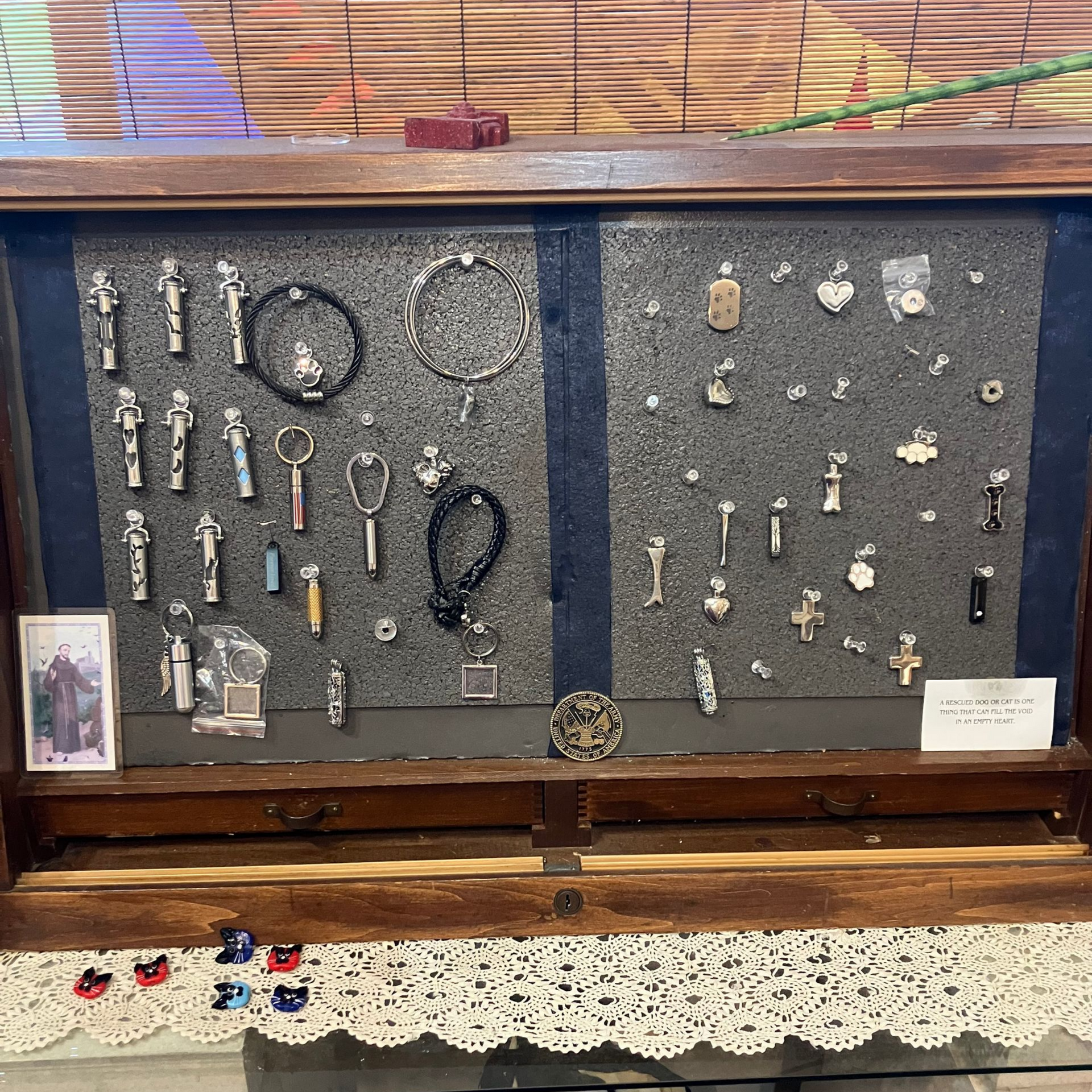 Wooden display case with assorted small metal tools and trinkets on dark backing, above a lace tablecloth