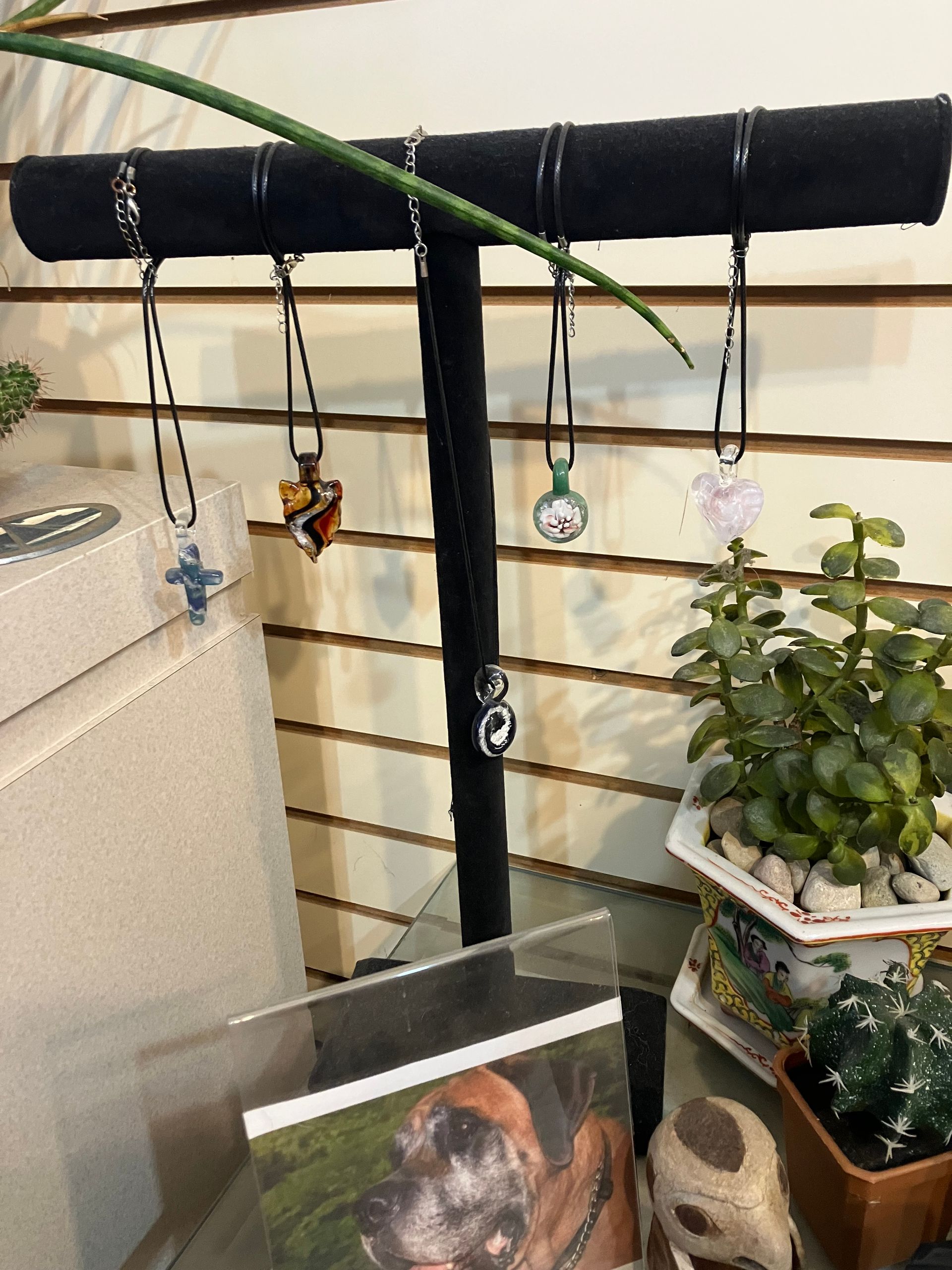 Black T-shaped bird perch with hanging toys and a photo, beside a potted plant on a shelf