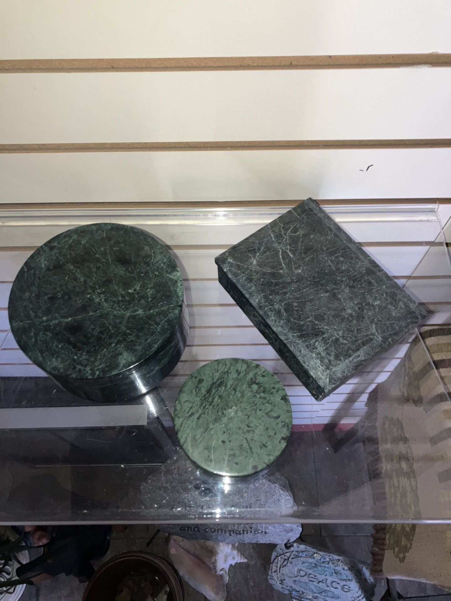 Three green textured geometric objects on a glass table against a striped wall. Three green textured geometric objects on a glass table against a striped wall.