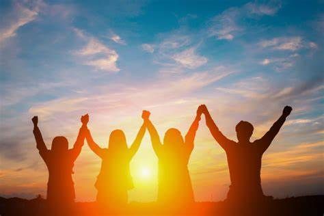 silhouette of people at sunrise all holding hands in the air