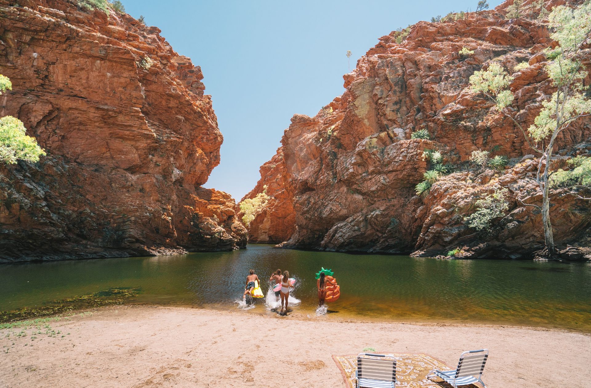 A group of people are standing on a beach next to a river.