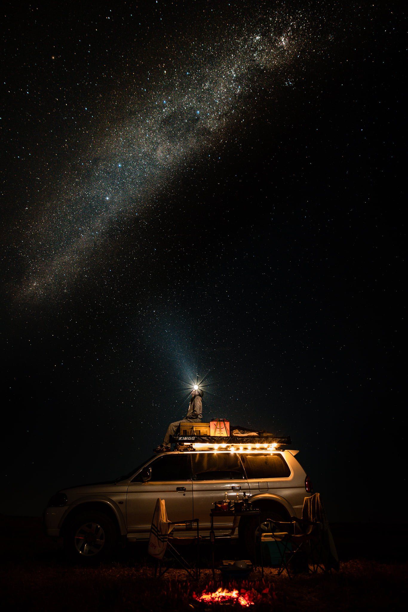 A car is parked under a starry sky at night.