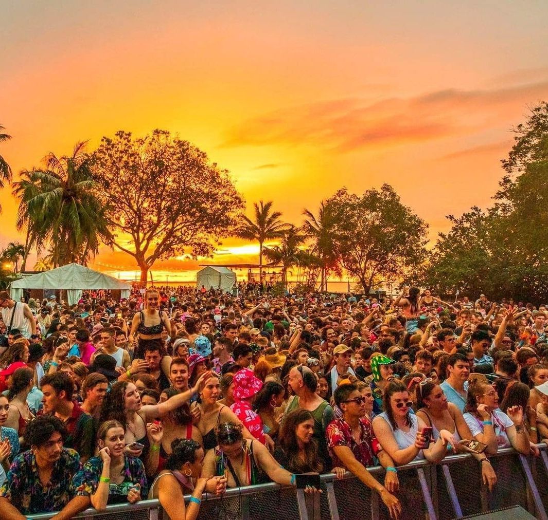 A large crowd of people are watching a concert at sunset.