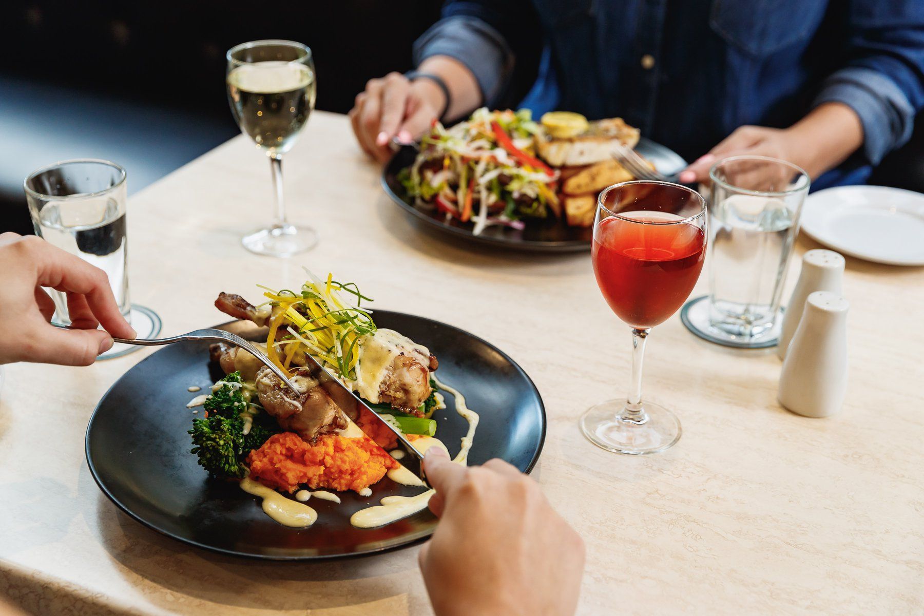 A couple is sitting at a table eating food and drinking wine.