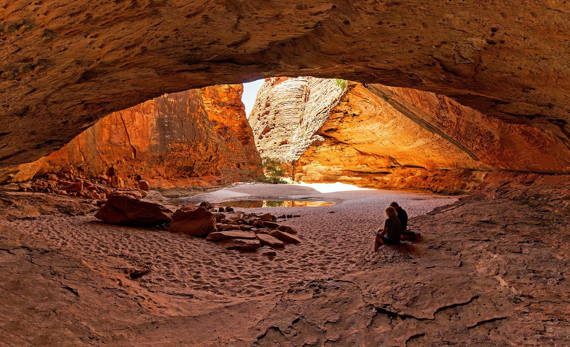 A person is sitting in a cave looking out over a body of water.