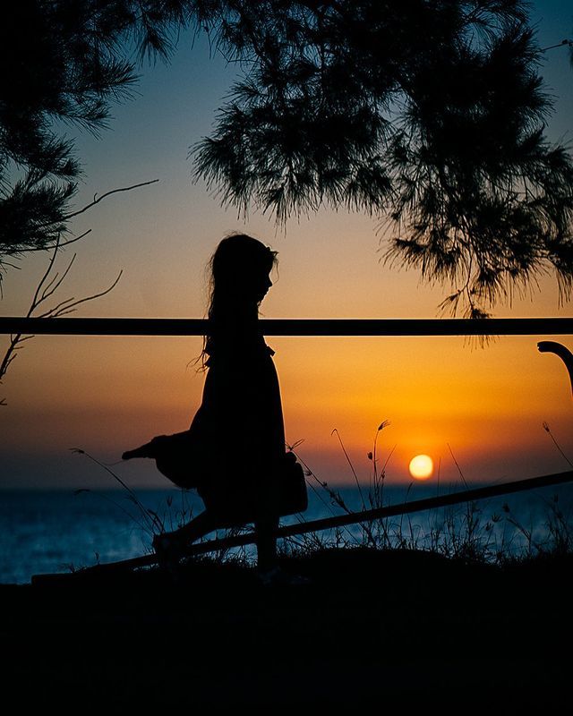 A silhouette of a woman standing next to a railing at sunset.
