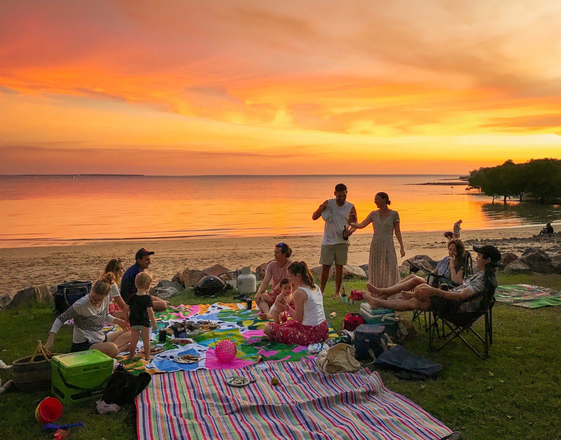 A group of people are having a picnic on the beach at sunset.