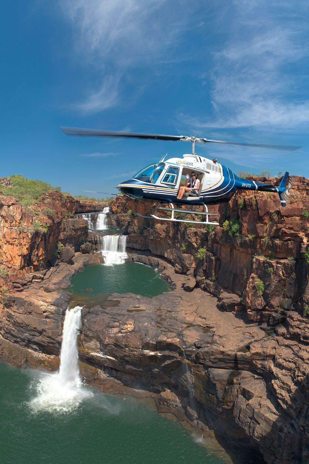A helicopter is flying over a waterfall in the middle of a canyon.
