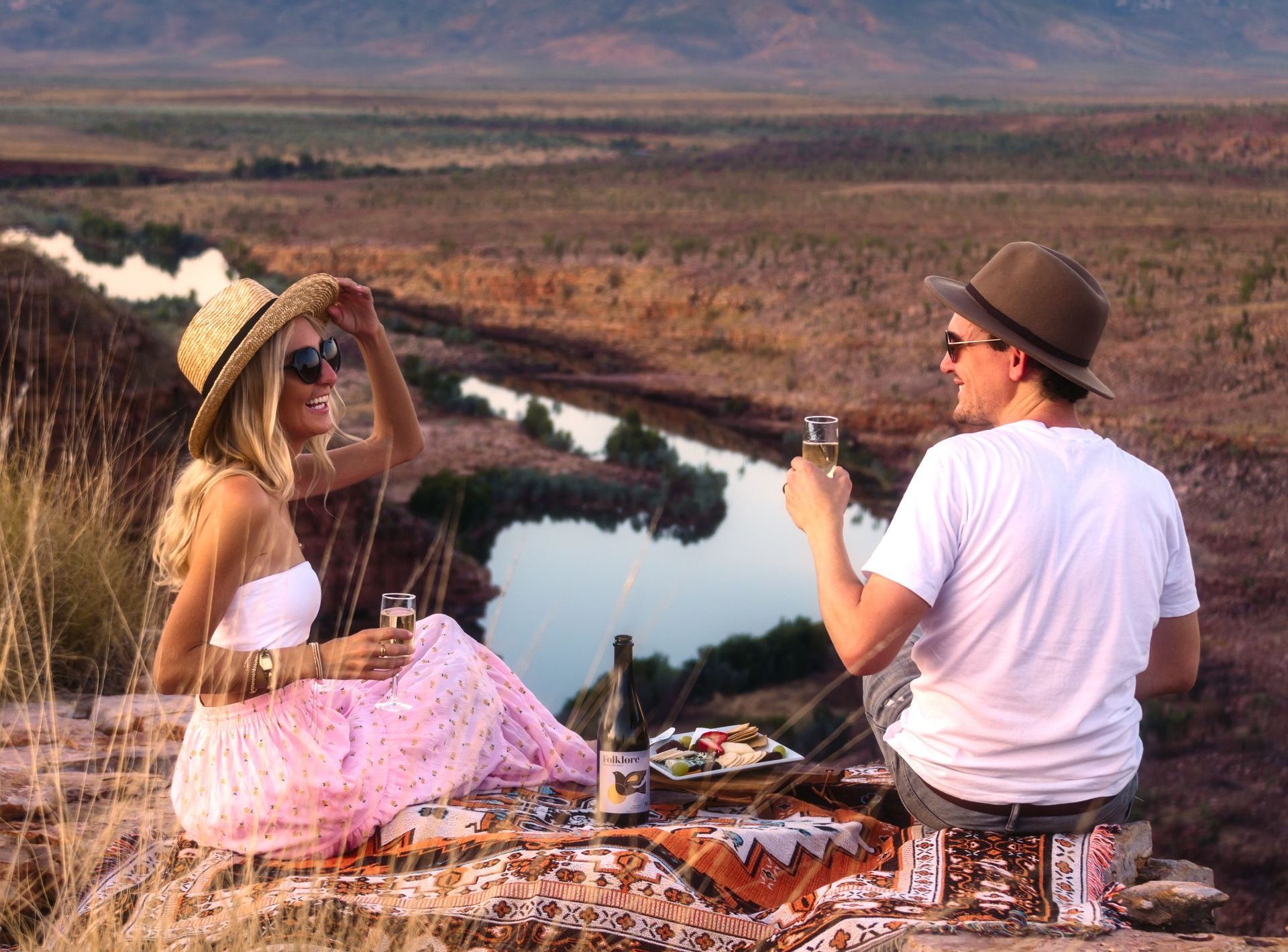 A man and a woman are having a picnic on top of a hill overlooking a river.