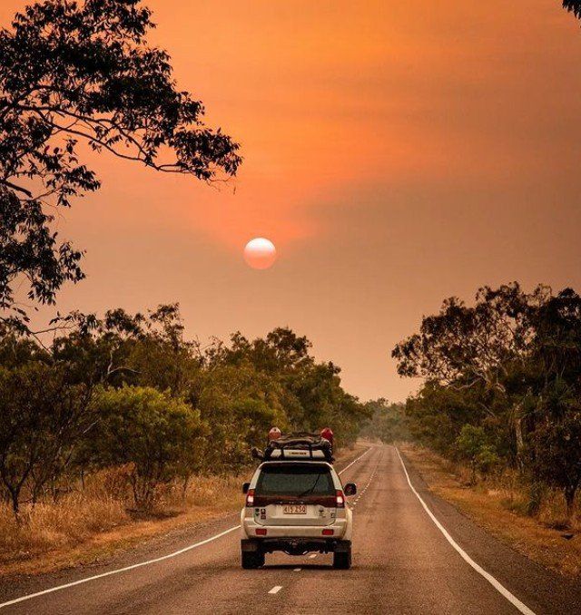 A car is driving down a road with a sunset in the background