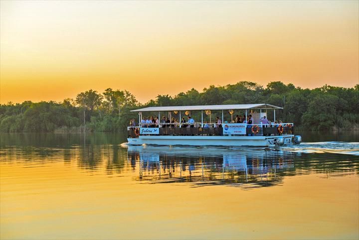 A boat with people on it is floating on a lake at sunset.