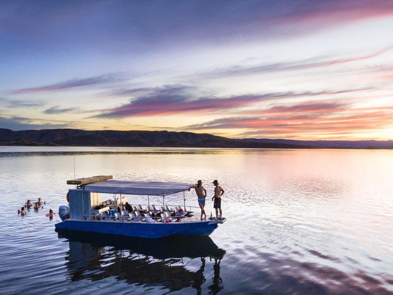 A group of people are standing on a boat in the middle of a lake at sunset.