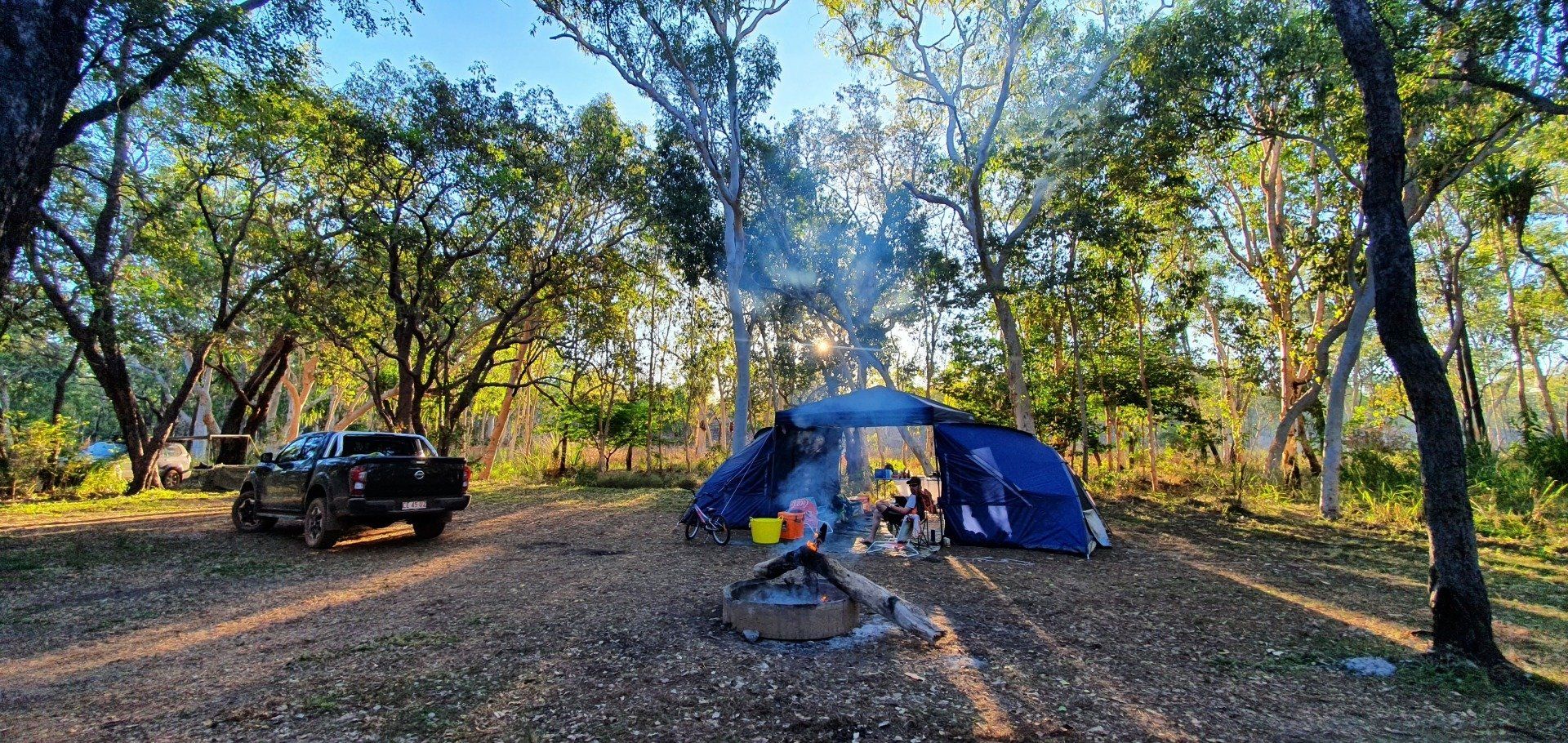 A truck is parked in front of a tent in the woods.