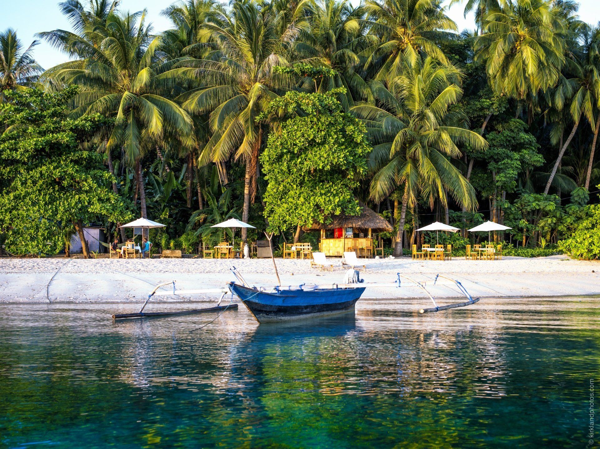 A boat is floating on the water near a beach surrounded by palm trees.