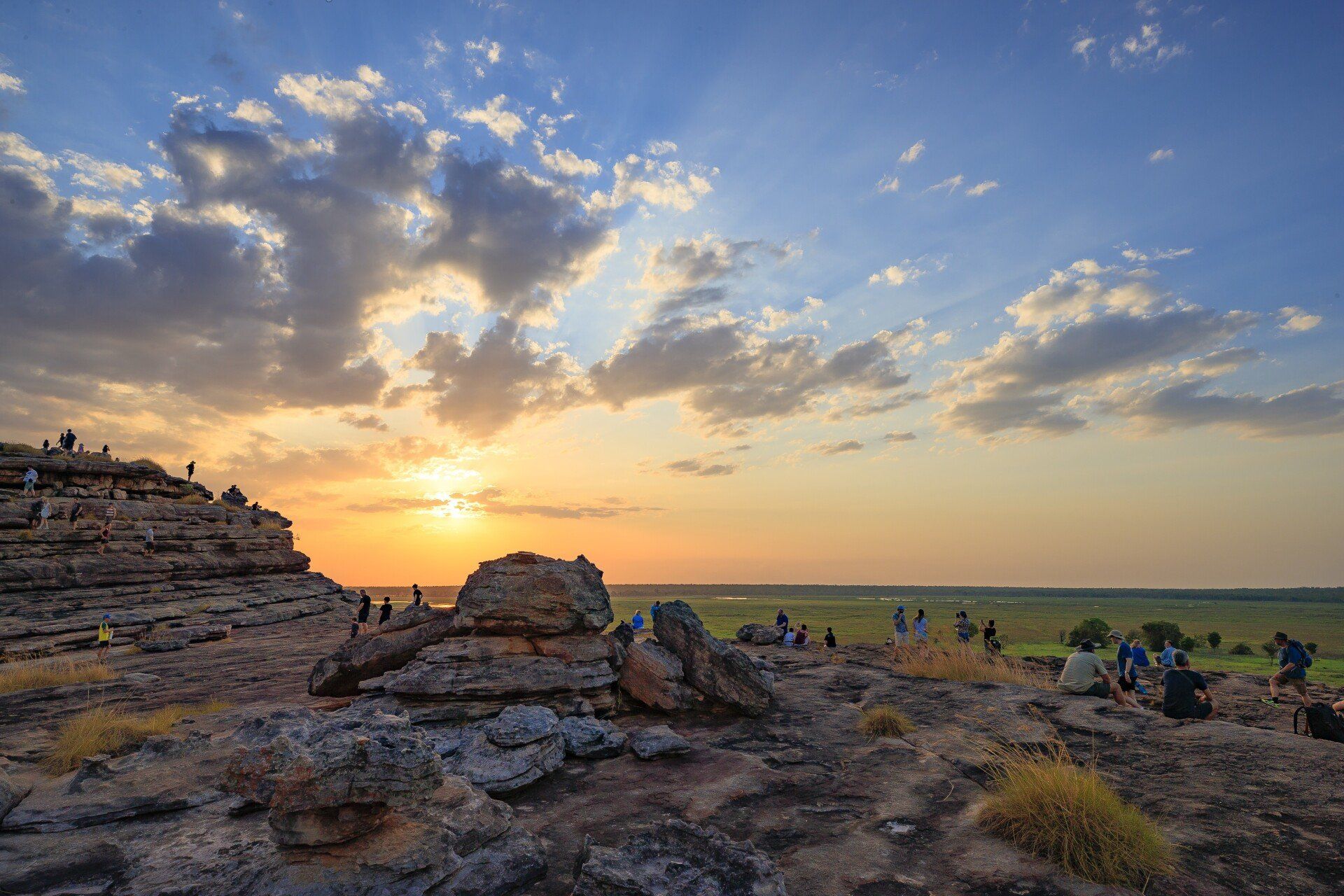 A group of people are sitting on top of a rocky hill at sunset.