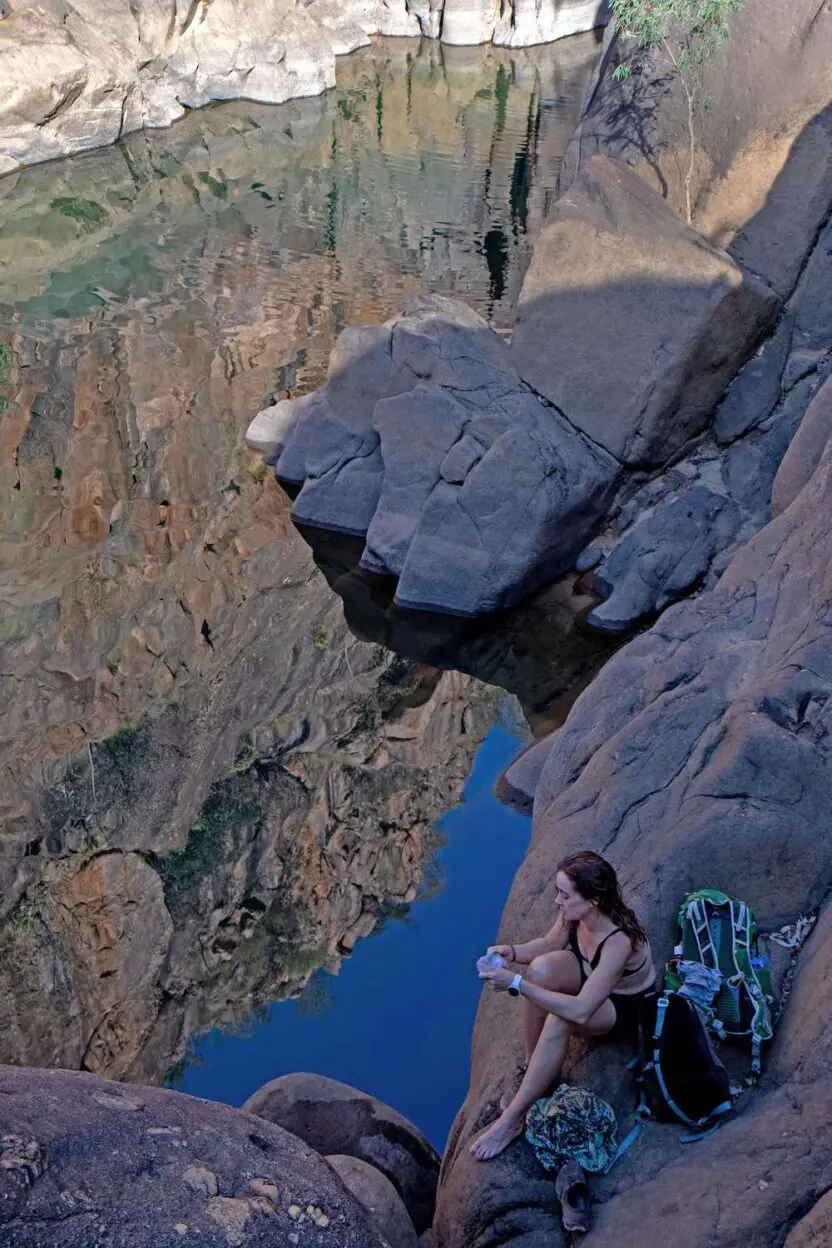 A woman is sitting on a rock near a body of water.
