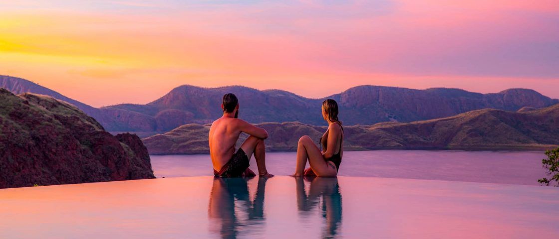 A man and a woman are sitting on the edge of an infinity pool.
