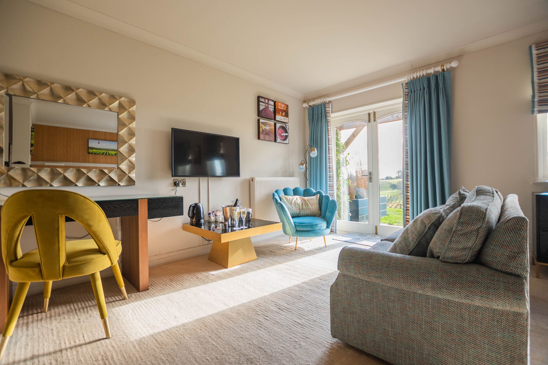 A bright living room with a yellow chair, teal accents, and a gray sofa. French doors lead to an outdoor view.