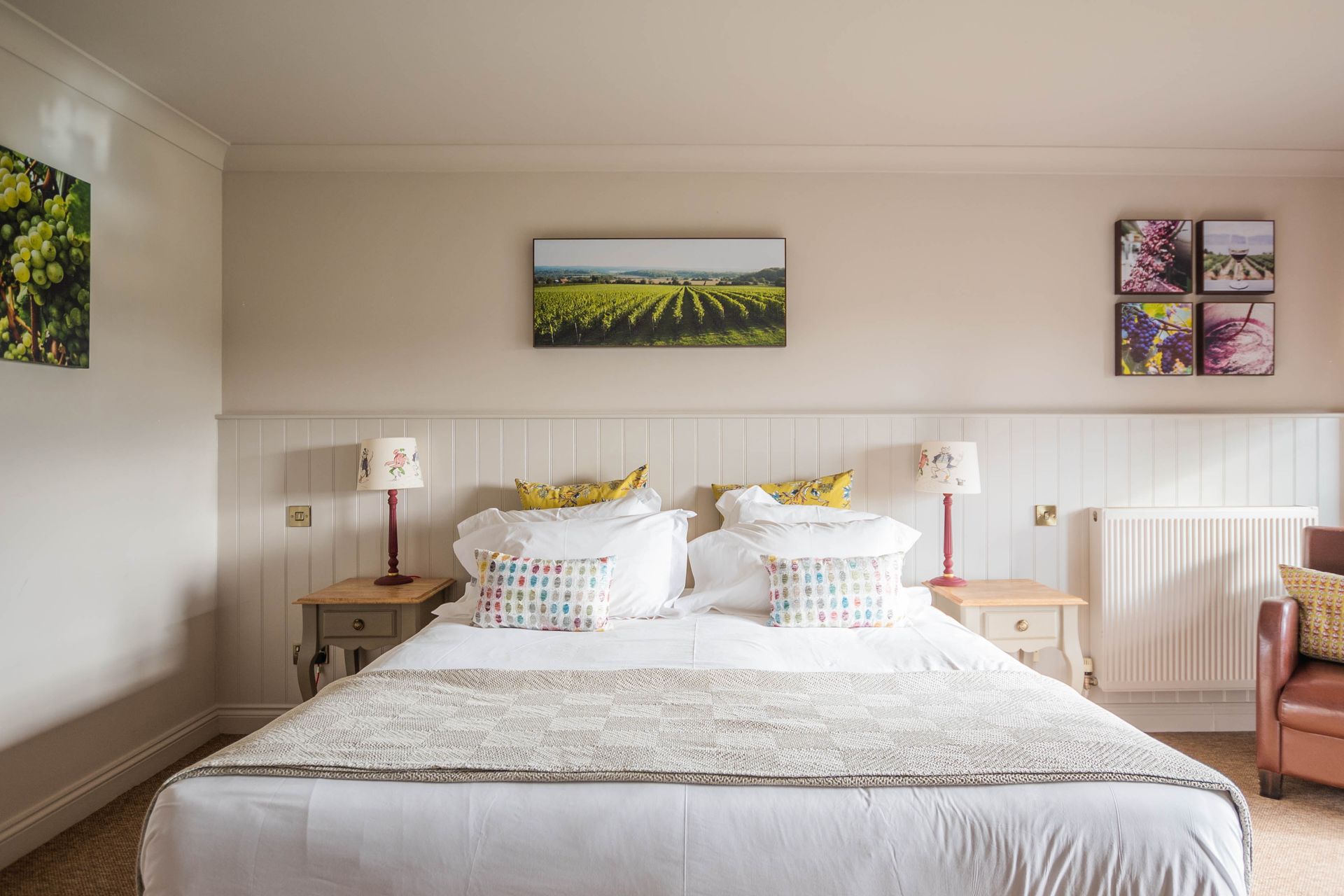 Bedroom with a white bed, two bedside tables with lamps, and artwork above the bed featuring a vineyard and flowers.