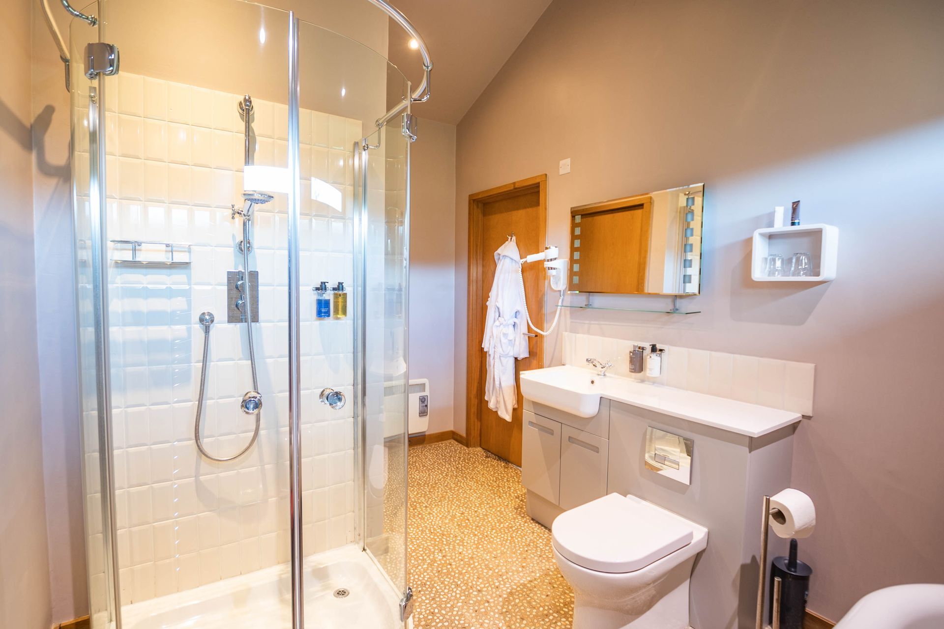 Modern bathroom with glass shower, toilet, sink, mirror, and bathrobe. Beige, gray, and white color scheme.