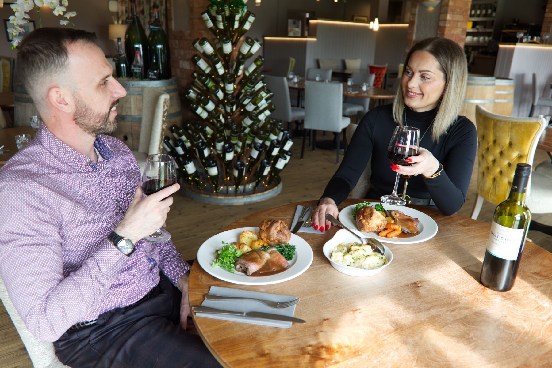 A wooden cutting board topped with food and a glass of wine on a wooden table.