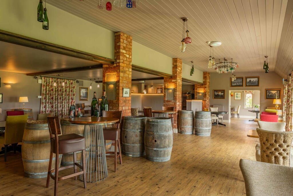 Interior of a bar/restaurant with wooden floors, barrels used as tables, and brick columns.