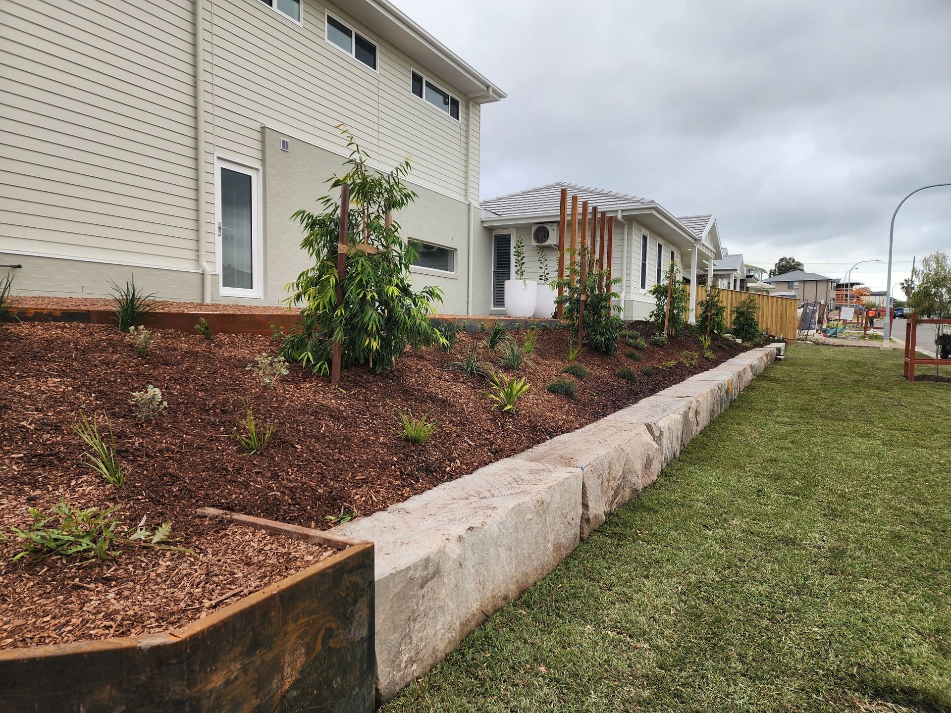 A lush green lawn with a wooden fence and flowers in the background — Green Envy Landscape & Garden Services In Cameron Park NSW