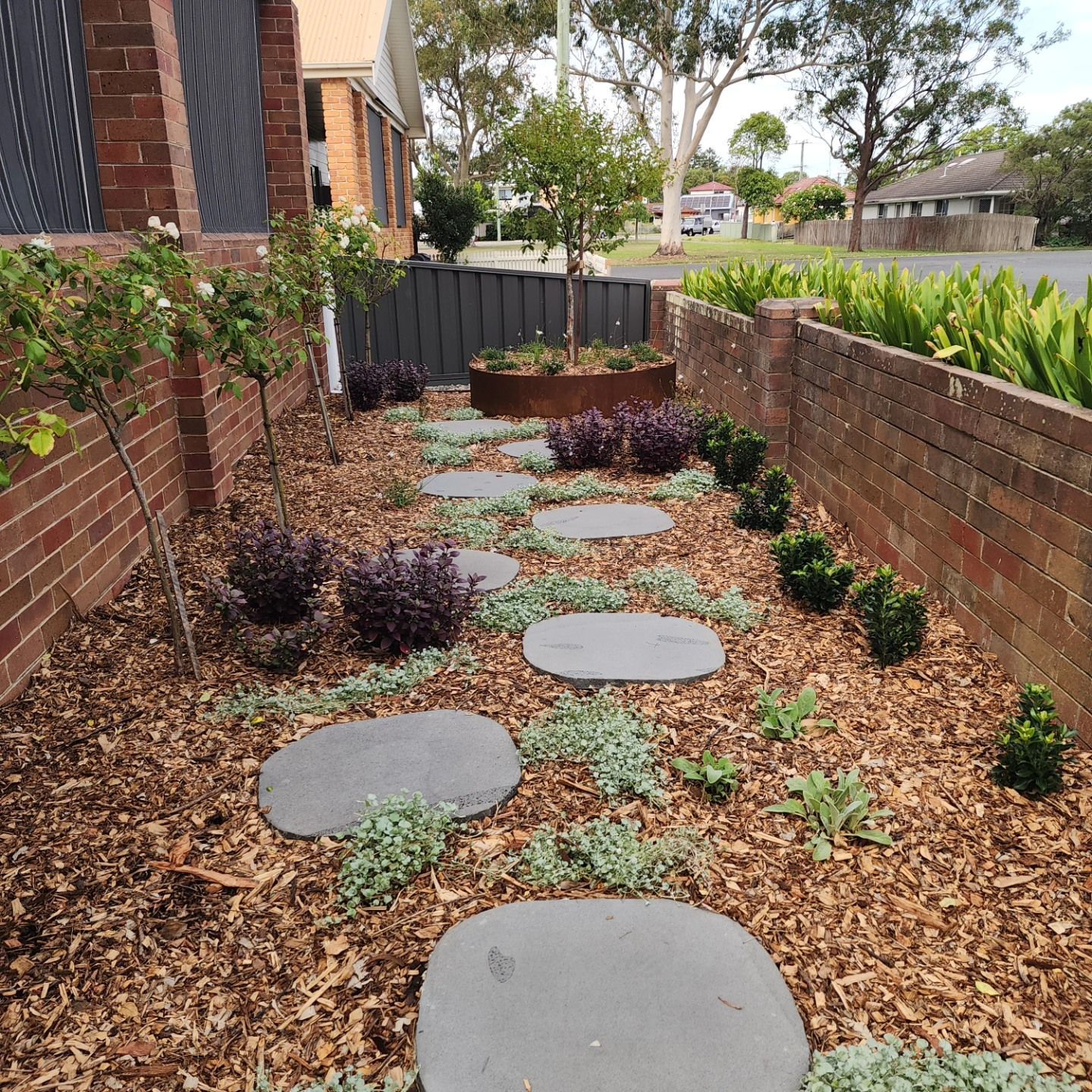 A Garden With A Brick Wall And Potted Plants — Green Envy Landscape & Garden Services In Cameron Park NSW