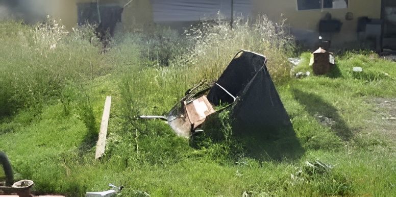 A broken chair is sitting in the grass in front of a house.