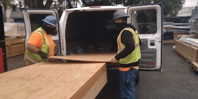Two construction workers are loading wood into a van.