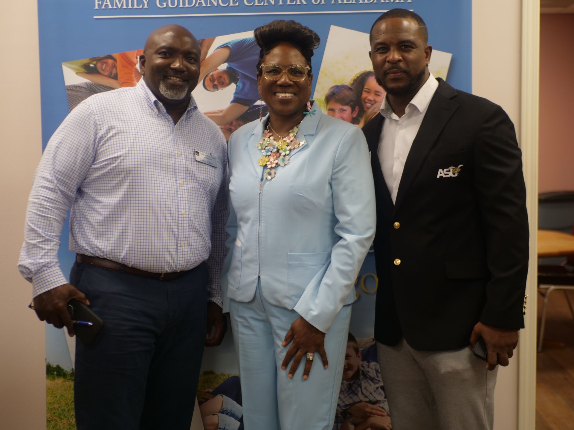 Three people are posing for a picture in front of a sign that says family guidance