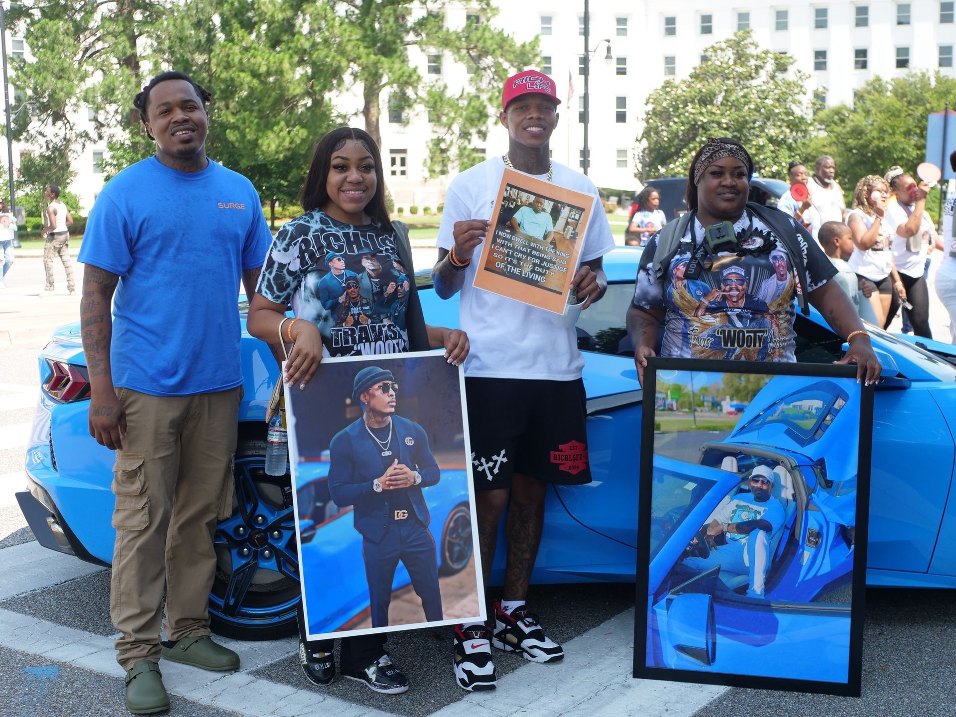 A group of people standing in front of a blue car holding pictures.