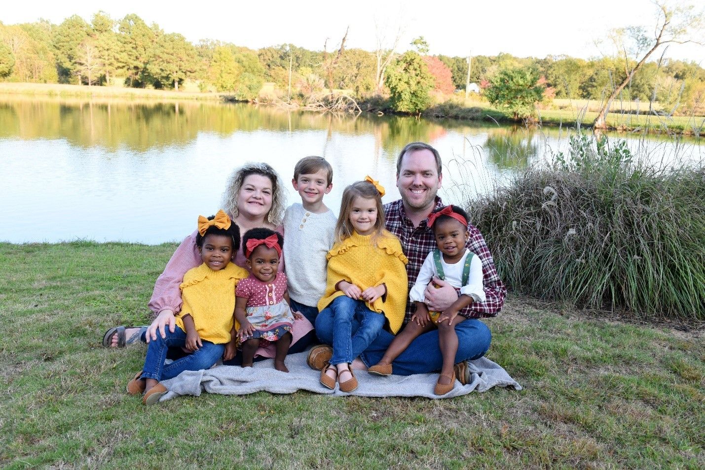 A family is sitting on a blanket in front of a lake.
