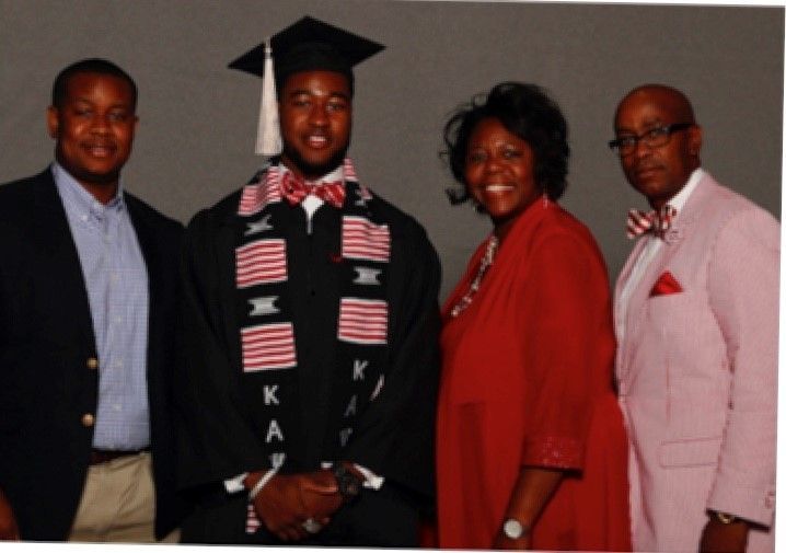 A man in a graduation cap and gown poses with his family