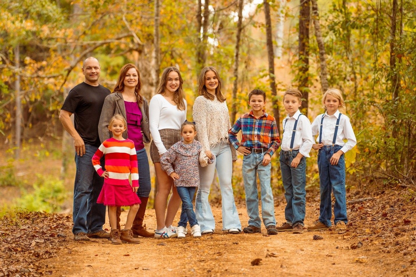 A large family is posing for a picture in the woods.