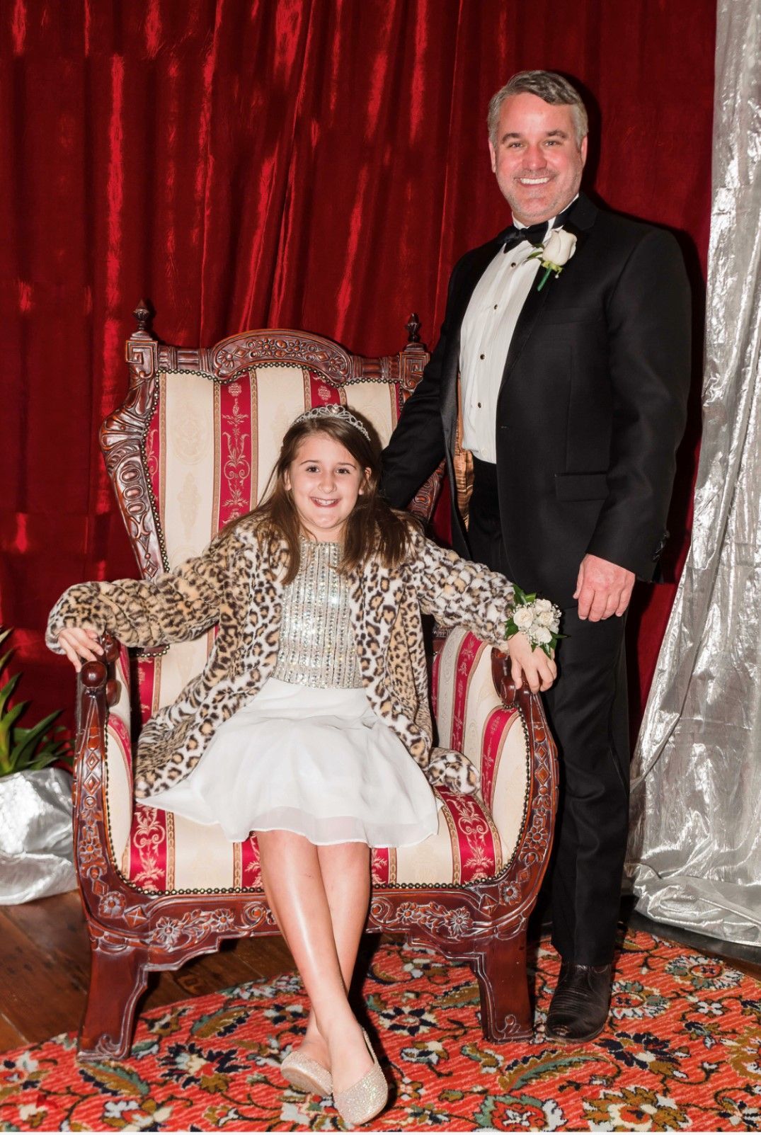 A man in a tuxedo is standing next to a little girl sitting in a chair.