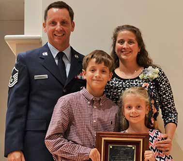 A man in a military uniform is standing next to a woman and two children holding a plaque.