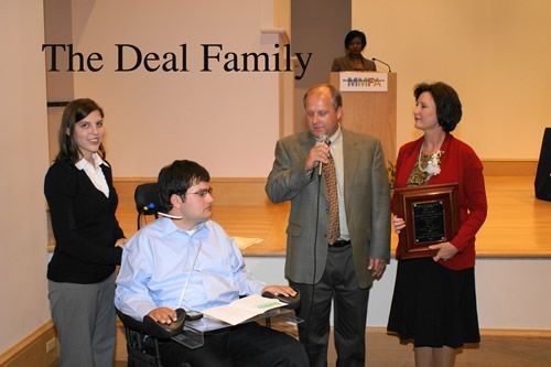 A man in a wheelchair is receiving an award from the deal family