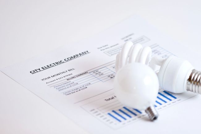 Lampadina su un report finanziario con grafico a barre blu e calcolatrice, a simboleggiare i costi energetici.