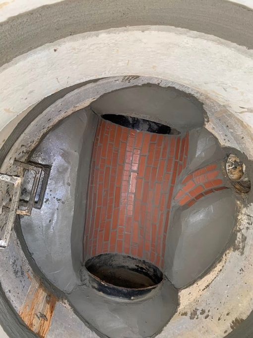 Top-down view of a circular concrete shaft with a red brick inner wall and metal fittings